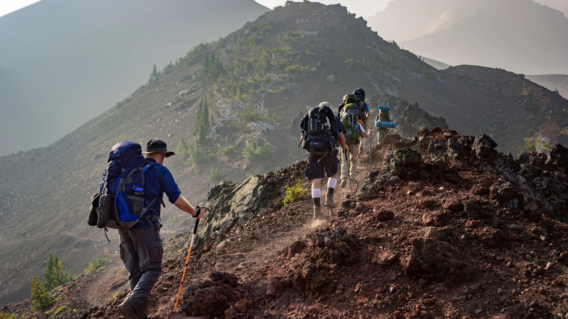 The golden hues of a sunrise illuminate the path as trekkers make their way up a Balinese mountain. This scene captures the serene beauty and physical exertion of a sunrise trekking adventure in Bali.